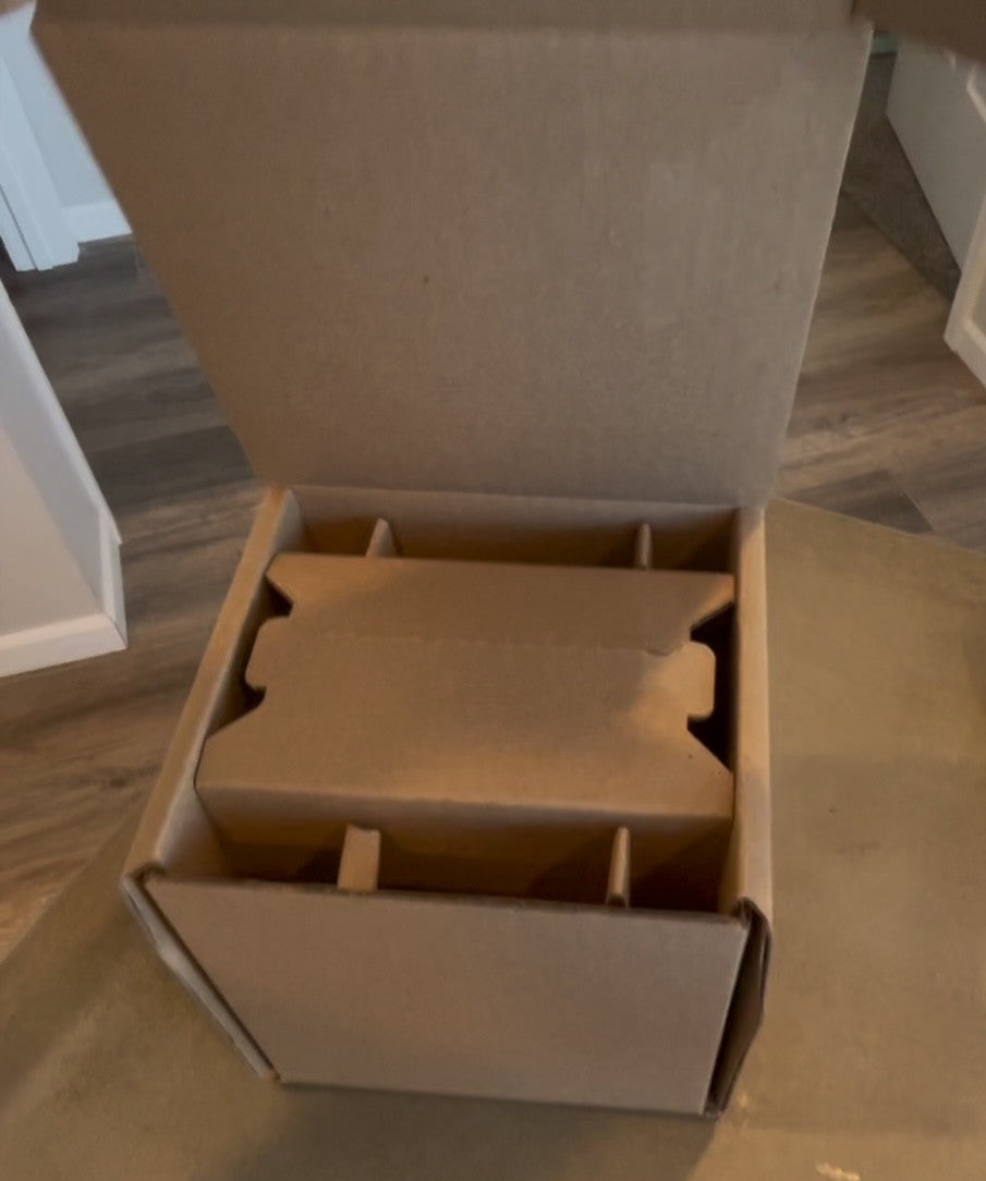 Open cardboard box on a wooden floor with a small object inside